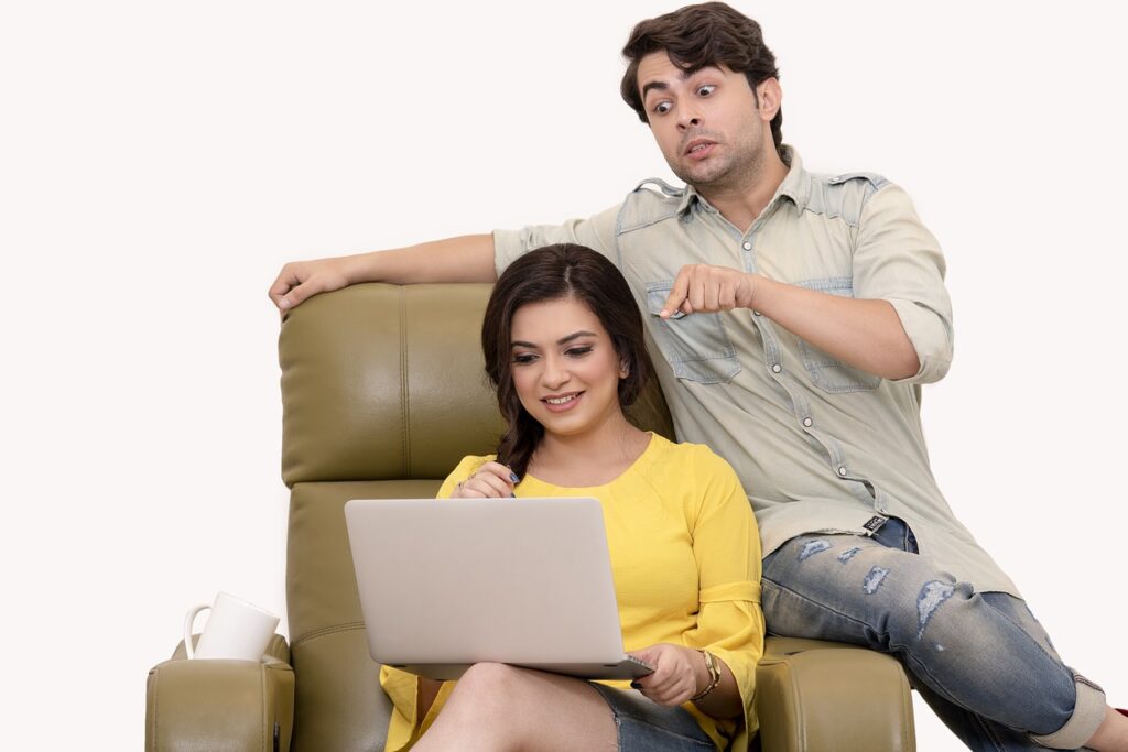Paar sitzt auf Sessel und Armlehne und er gestikuliert, während beide auf den Laptop schauen